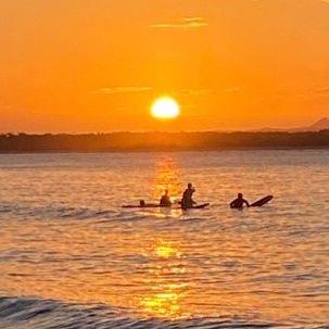 Noosa sunset over ocean, surfers in the foreground